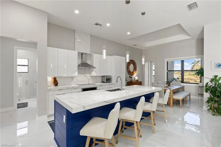Kitchen with white cabinets, decorative light fixtures, modern cabinets, light stone countertops, and a large island