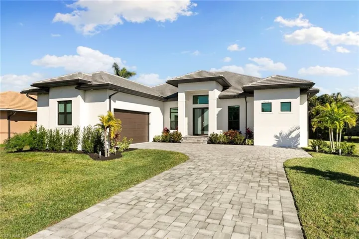 Prairie-style home with a garage, decorative driveway, stucco siding, and a front lawn