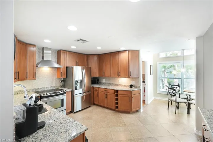 Kitchen with stainless steel appliances, brown cabinets, visible vents, and wall chimney exhaust hood