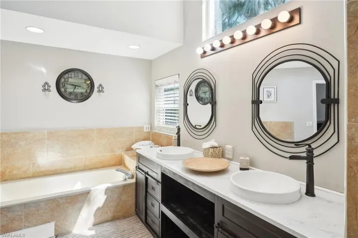 Bathroom featuring a bath, double vanity, a sink, and recessed lighting