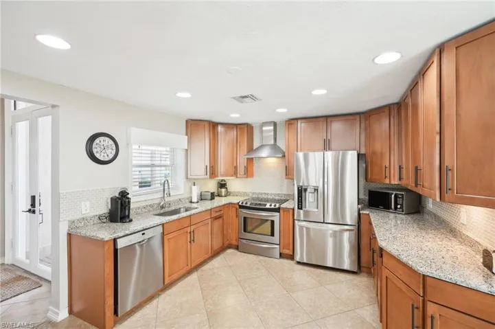 Kitchen with visible vents, appliances with stainless steel finishes, a sink, light stone countertops, and wall chimney exhaust hood