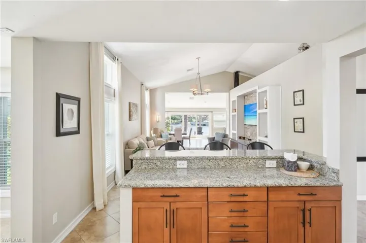 Kitchen featuring brown cabinets, open floor plan, light tile patterned flooring, vaulted ceiling, and light stone countertops