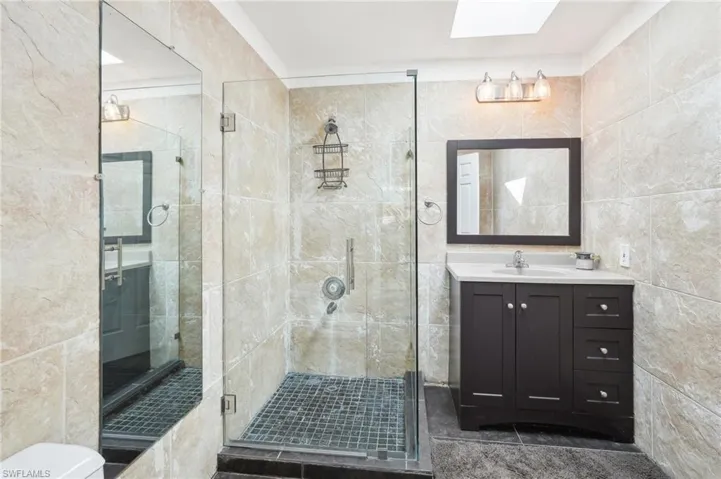 Full bathroom with a skylight, tile walls, toilet, a stall shower, and vanity