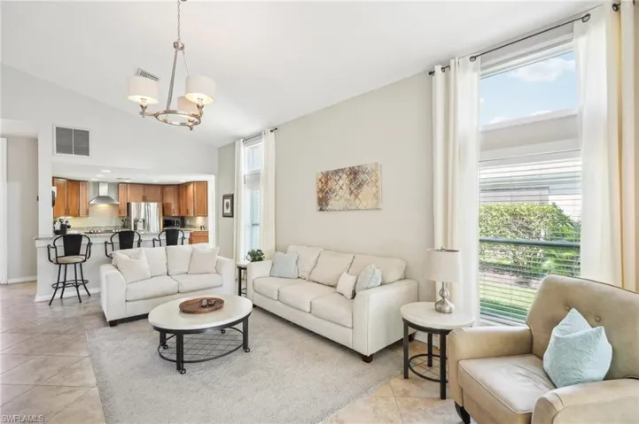 Living area with high vaulted ceiling, light tile patterned flooring, visible vents, and a notable chandelier