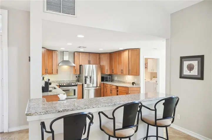 Kitchen featuring visible vents, appliances with stainless steel finishes, wall chimney range hood, separate washer and dryer, and a sink