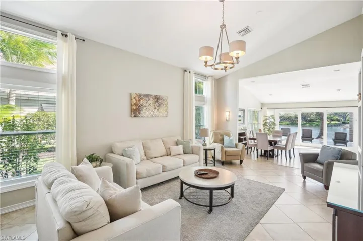 Living room featuring lofted ceiling, light tile patterned flooring, visible vents, plenty of natural light, and an inviting chandelier
