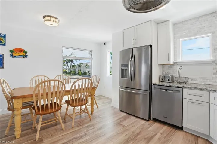 Kitchen with stainless steel appliances, white cabinets, light stone countertops, backsplash, and light wood-style flooring - Virtually Edited Image