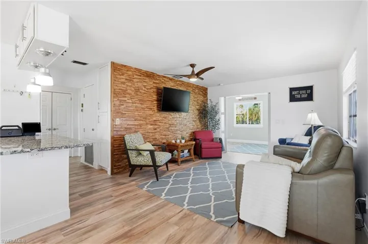 Living room with ceiling fan, light wood finished floors, and an accent wall - Virtually Edited Image
