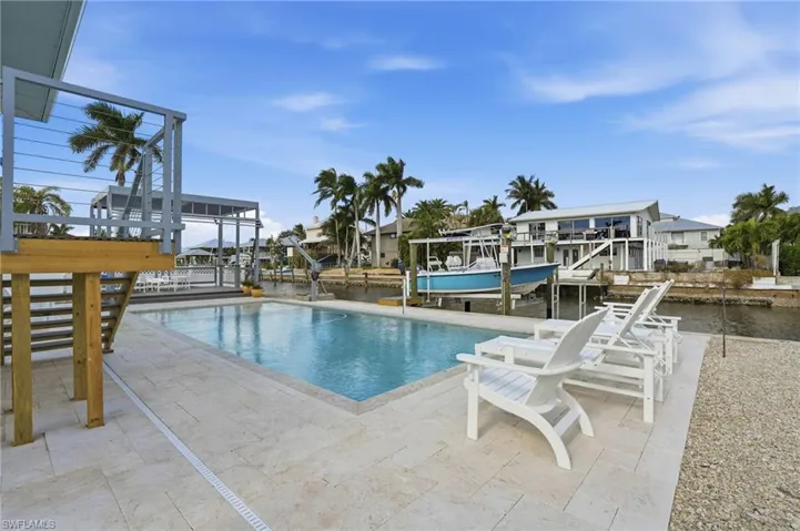 Swimming pool with boat lift, a dock, a patio, and a water view - Virtually Edited Image