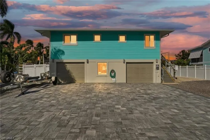 Coastal home featuring decorative driveway, stairway, and an attached garage - Virtually Edited Image