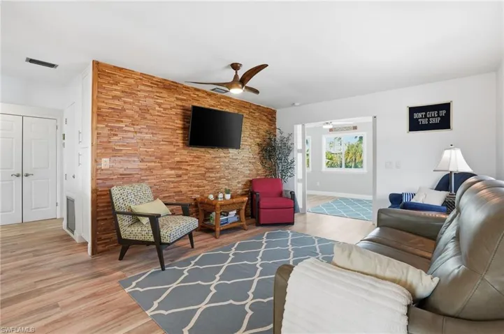 Living area with ceiling fan, an accent wall, and light wood-style flooring - Virtually Edited Image