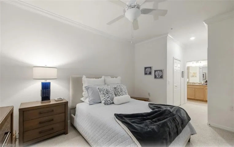Primary Bedroom with light carpet, ornamental molding, a walk-in closet, a ceiling fan, and ensuite bathroom