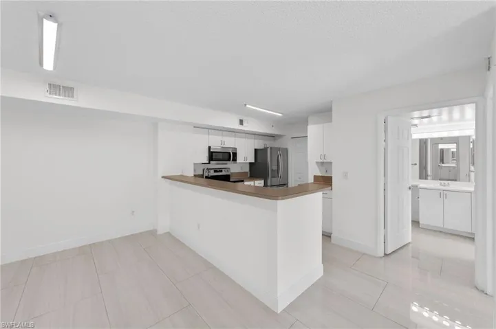 Kitchen with a peninsula, white cabinetry, appliances with stainless steel finishes, a textured ceiling, and light tile patterned floors