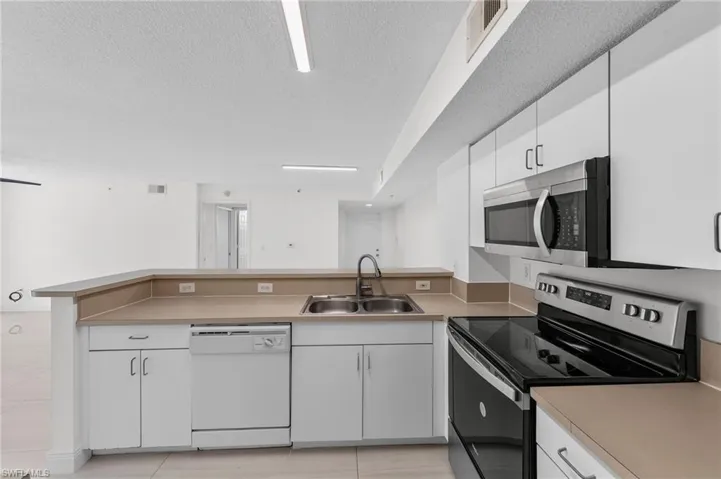 Kitchen featuring stainless steel appliances, white cabinetry, a textured ceiling, a peninsula, and light countertops
