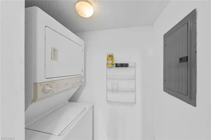 Laundry room featuring a textured ceiling, electric panel, and estacked washer and dryer