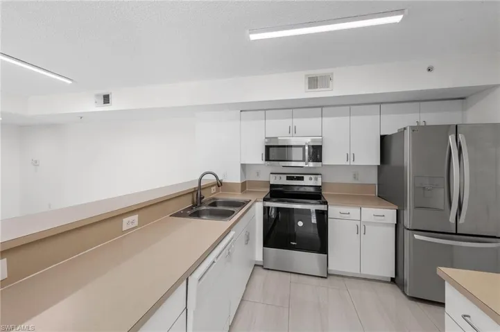 Kitchen with appliances with stainless steel finishes, white cabinets, light countertops, a textured ceiling, and light tile patterned floors