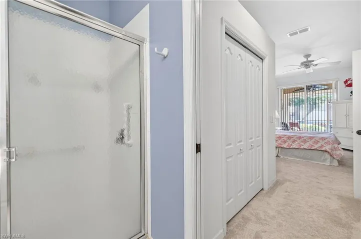 Full bathroom featuring ensuite bath, a shower stall, light colored carpet, ceiling fan, and a closet