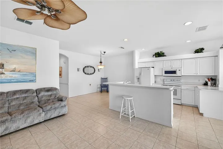 Kitchen featuring light countertops, arched walkways, white appliances, white cabinetry, and a center island