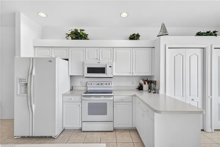 Kitchen featuring white appliances, light countertops, a peninsula, light tile patterned floors, and white cabinetry