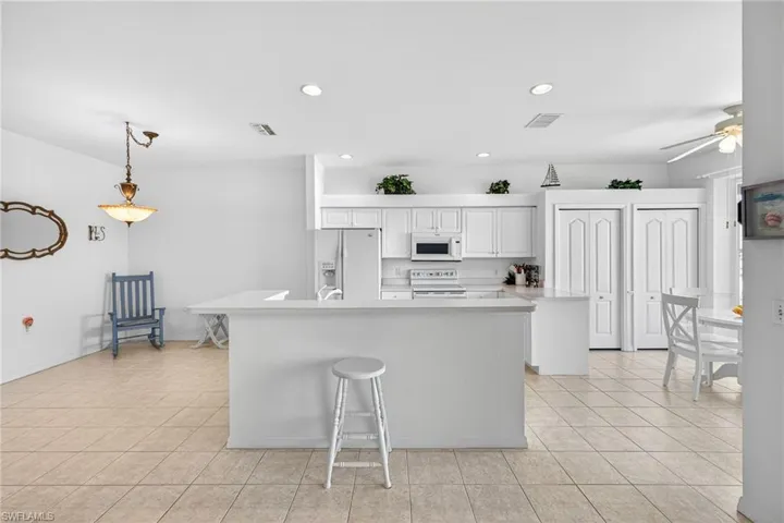 Kitchen with white cabinets, light countertops, white appliances, and a ceiling fan
