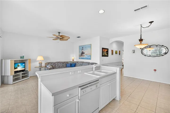 Kitchen with arched walkways, open floor plan, white cabinetry, white dishwasher, and a ceiling fan