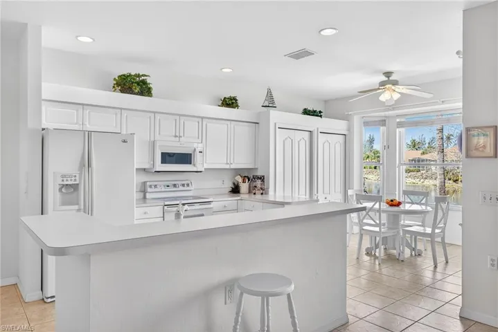 Kitchen with light countertops, white appliances, a kitchen bar, ceiling fan, and light tile patterned floors