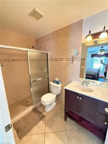 Ensuite bathroom with vanity, tile walls, a stall shower, and light tile patterned floors