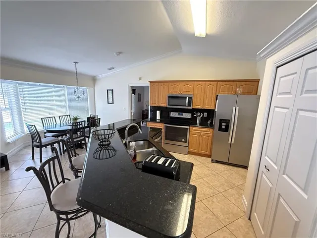 Kitchen with ornamental molding, lofted ceiling, appliances with stainless steel finishes, light tile patterned floors, and decorative light fixtures