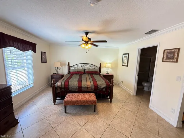Bedroom with light tile patterned flooring, a textured ceiling, ornamental molding, and ceiling fan