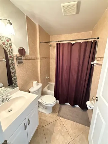 Bathroom with tile walls, vanity, shower / tub combo, and light tile patterned floors