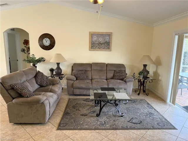 Tiled living area featuring crown molding, lofted ceiling, and arched walkways