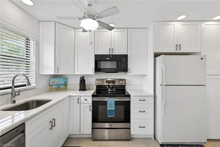 Kitchen with stainless steel appliances, white cabinets, recessed lighting, light stone counters, and a ceiling fan