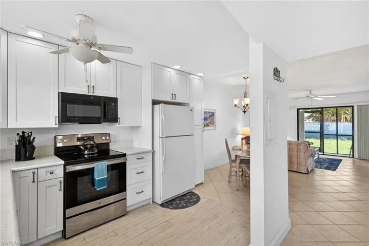 Kitchen featuring ceiling fan, stainless steel electric range, freestanding refrigerator, black microwave, and white cabinets