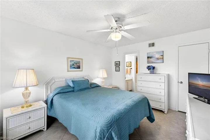 Bedroom with a textured ceiling, a ceiling fan, ensuite bathroom, and light tile patterned flooring