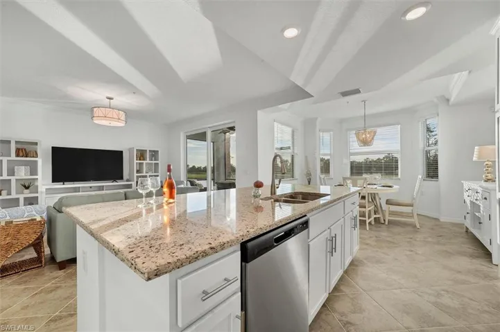 Kitchen with open floor plan, white cabinetry, stainless steel dishwasher, ornamental molding, and light stone counters