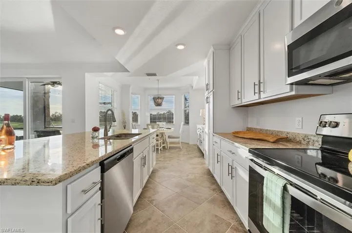 Kitchen with stainless steel appliances, white cabinetry, an island with sink, light stone counters, and recessed lighting