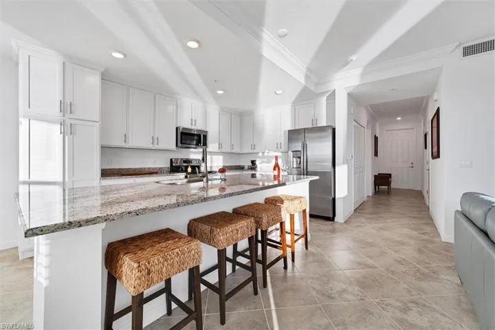 Kitchen with light stone countertops, a kitchen breakfast bar, white cabinets, appliances with stainless steel finishes, and a kitchen island with sink