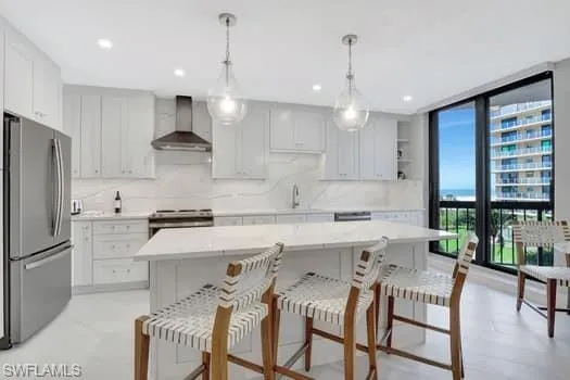 Kitchen featuring stainless steel appliances, white cabinets, hanging light fixtures, wall chimney range hood, and a center island