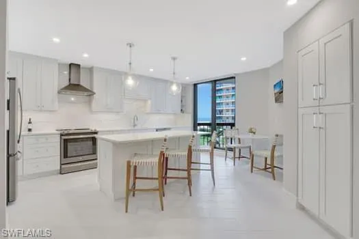 Kitchen with floor to ceiling windows, light countertops, hanging light fixtures, appliances with stainless steel finishes, and wall chimney range hood