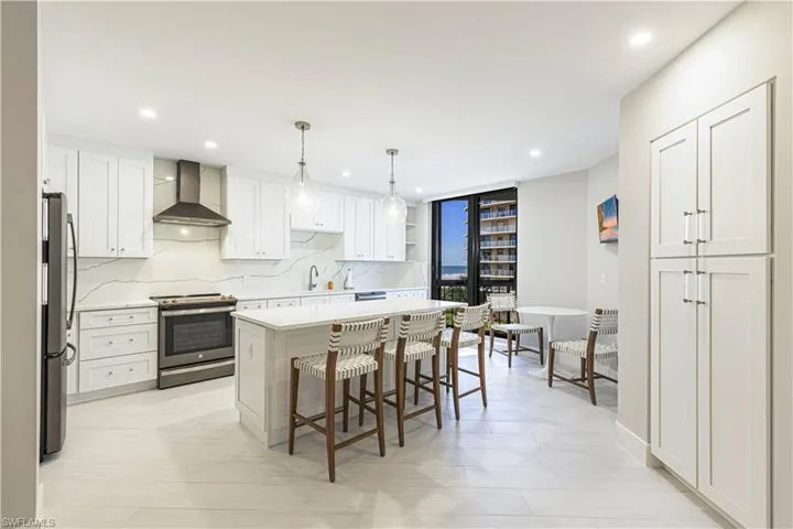 Kitchen with white cabinetry, wall chimney exhaust hood, hanging light fixtures, stainless steel appliances, and a kitchen island
