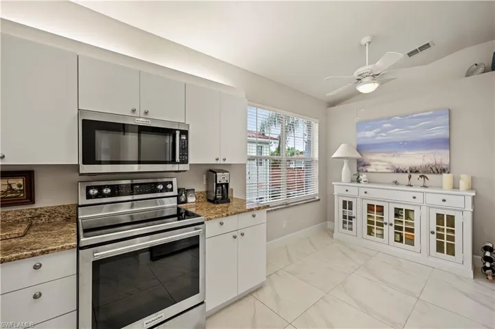 Kitchen featuring light tile patterned floors, dark stone countertops, white cabinetry, ceiling fan, and stainless steel appliances