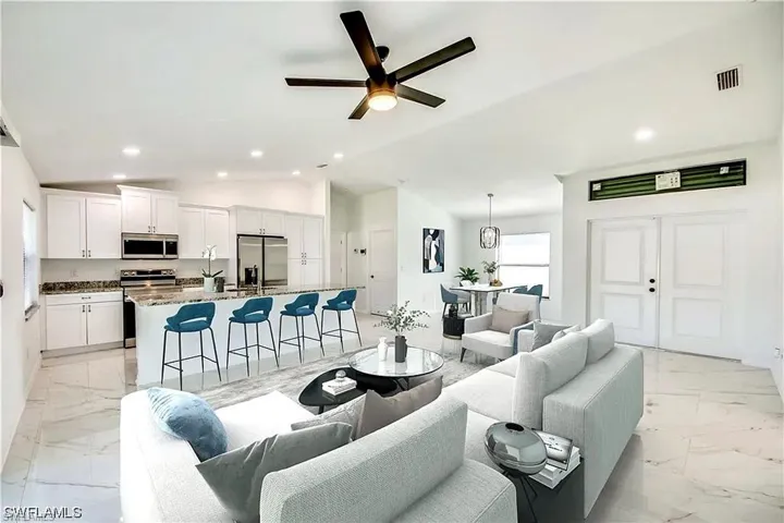Open-concept living space featuring a kitchen island with seating, stainless steel appliances, white cabinetry, and large format tile flooring