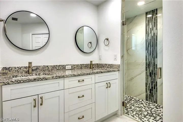 Dual vanity with granite countertop, white cabinetry, and gold-tone fixtures