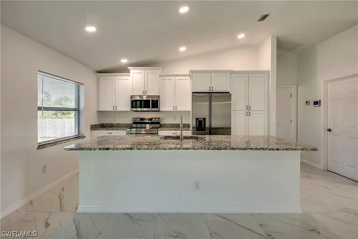 Kitchen featuring white shaker cabinetry, stainless steel appliances, granite countertops, a large island with sink, and recessed lighting