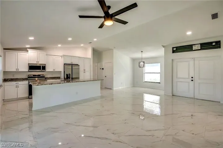 Open-concept living space with large format tile flooring, a kitchen island with stone countertop, white shaker cabinetry, and stainless steel appliances