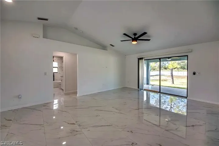 Spacious interior featuring vaulted ceilings, large format tile flooring, a contemporary ceiling fan, and sliding glass doors