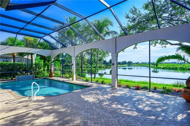 View of swimming pool featuring glass enclosure, a patio, and a water view