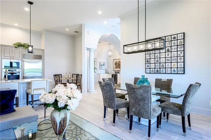 Dining room with a towering ceiling, ornate columns, ornamental molding, and light hardwood / wood-style flooring