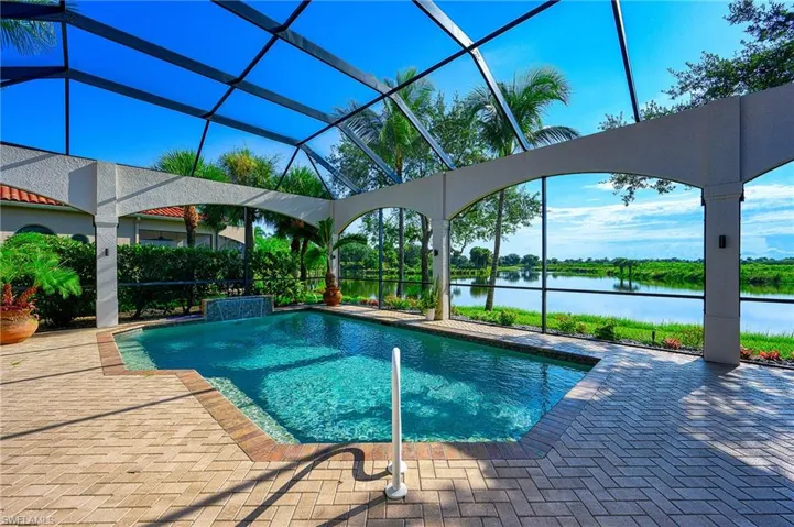 View of swimming pool featuring glass enclosure, a patio area, and a water view