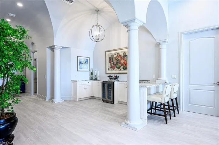 Quartz countertops, white cabinetry, wine cooler, pendant lighting, and bar seating